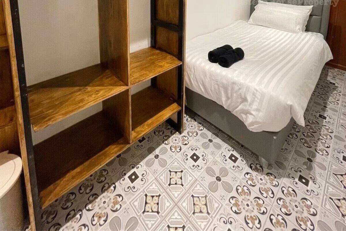 A bedroom with a bed, a wardrobe with multiple shelves, and patterned floor tiles.