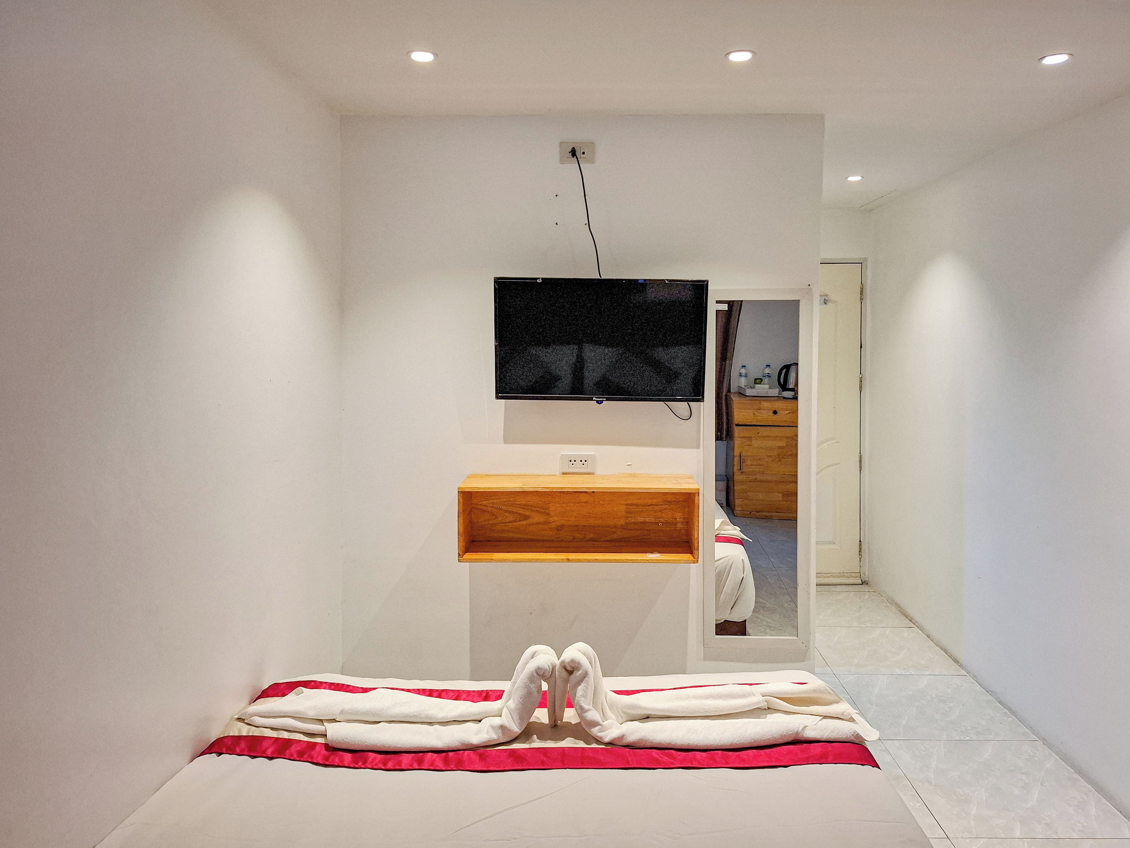A modern bathroom with a wooden vanity, a mirror, and a flat-screen TV mounted on the wall.