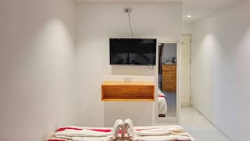 A modern bathroom with a wooden vanity, a mirror, and a flat-screen TV mounted on the wall.