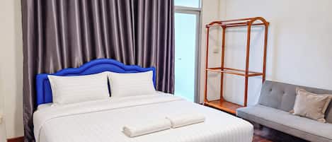 Een hotelkamer met een bed, een grijze bank, een houten wandplank en een raam met gordijnen.