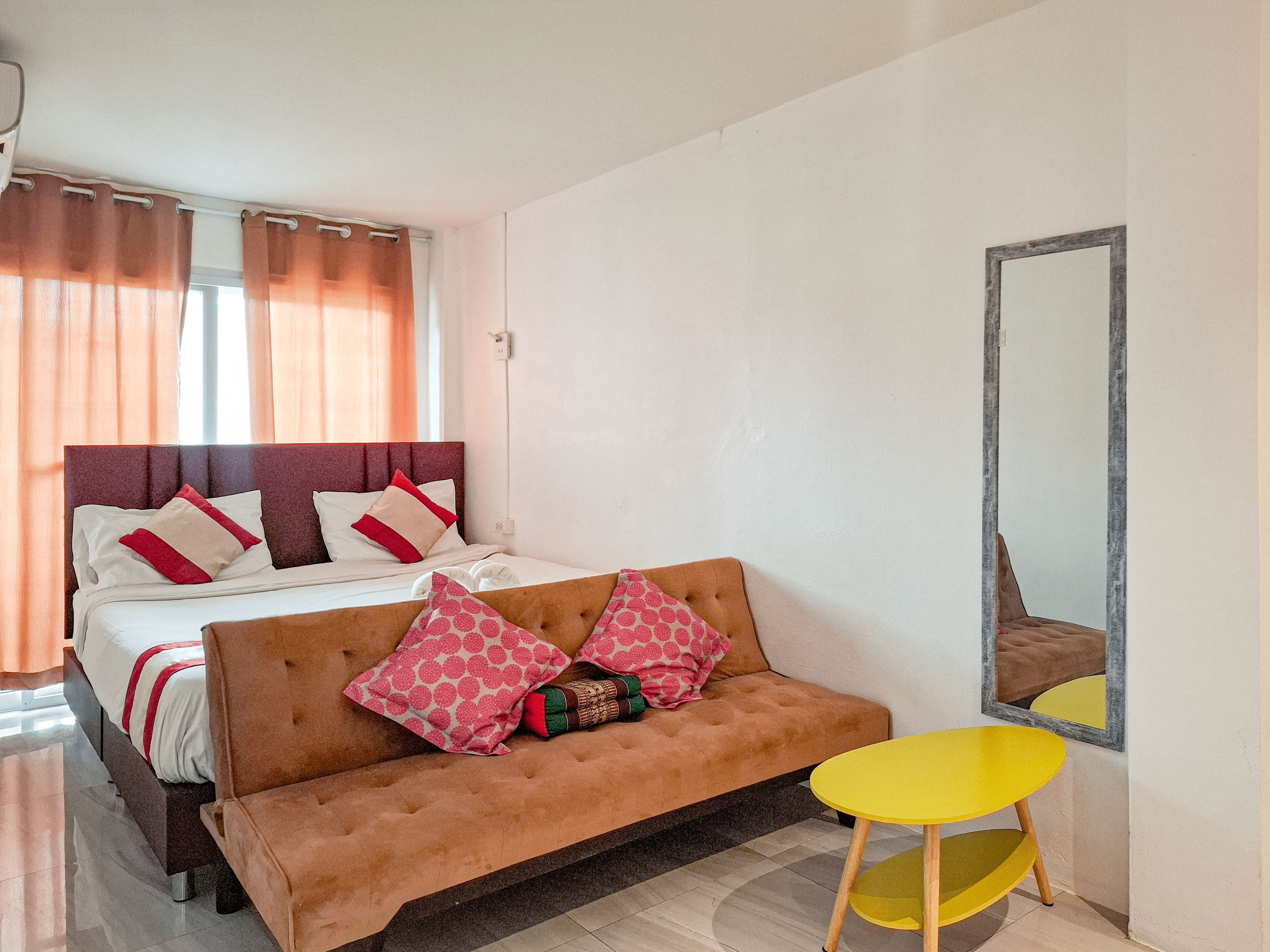 A bedroom with a bed, a sofa, a small table, and a mirror.