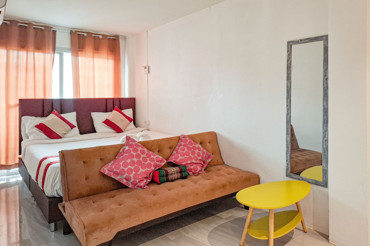 A bedroom with a bed, a sofa, a small table, and a mirror.