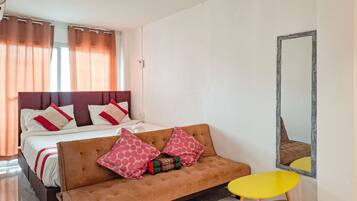 A bedroom with a bed, a sofa, a small table, and a mirror.