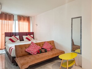 A bedroom with a bed, a sofa, a small table, and a mirror. - YOK Guesthouse Jomtien (Pattaya)