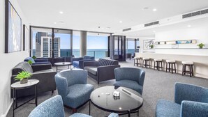 Uma área de estar moderna com assentos confortáveis, um bar e grandes janelas com vista para o oceano e a paisagem urbana.