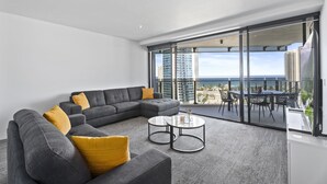 Uma sala de estar moderna com um sofá modular cinza, almofadas amarelas e uma mesa de centro de vidro.