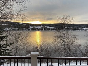 A lakeside view with a wooden railing, snow-covered ground, and buildings in the background.