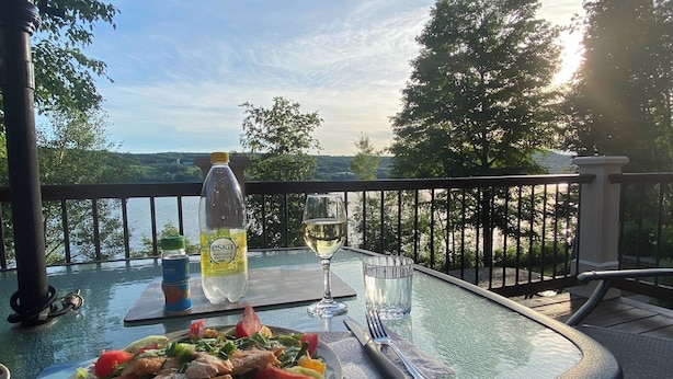 A table with a meal, a bottle of water, and a glass of wine on a balcony overlooking a lake. - La Chaumiere - Lakefront & Private Beach (Pohénégamook)