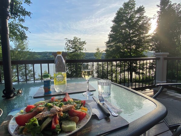 A table with a meal, a bottle of water, and a glass of wine on a balcony overlooking a lake.