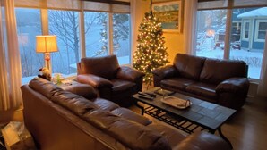 A cozy living room with leather couches, a coffee table, and a Christmas tree. - La Chaumiere - Lakefront & Private Beach (Pohénégamook)