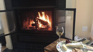 A fireplace with a glass door, a table with a plate of cheese and crackers, and a glass of wine. - La Chaumiere - Lakefront & Private Beach (Pohénégamook)