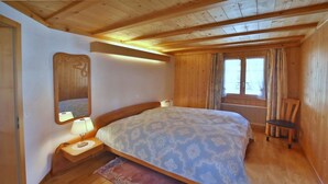 Une chambre à coucher aux murs lambrés, avec un lit, une table de chevet, une chaise et une fenêtre avec des rideaux.