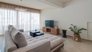 A modern living room with a beige sofa, a wooden TV stand, a black side table, and a potted plant.