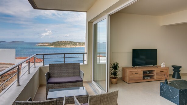 A balcony with a view of the sea, a sofa, a TV, and a wooden cabinet.