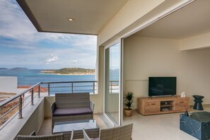 A balcony with a view of the sea, a sofa, a TV, and a wooden cabinet. - Oikies luxury apartment with Sea & Town View | private free parking area (Agios Nikolaos, Crete)