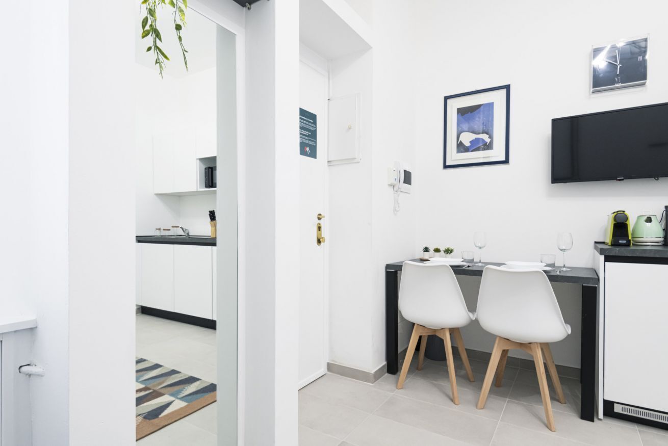 Una cocina moderna con armarios blancos, encimera negra y una zona de comedor con dos sillas blancas.