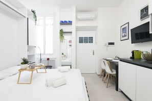 Moderni hotellihuone, jossa on sänky, yöpöytä ja pieni keittokomero.