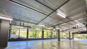 Un parking couvert avec des planchers en béton, des poutres métalliques et de grandes fenêtres qui laissent entrer la lumière naturelle.