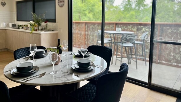 Un coin repas avec une table ronde dressée pour quatre personnes, de grandes fenêtres et une vue sur l’extérieur.