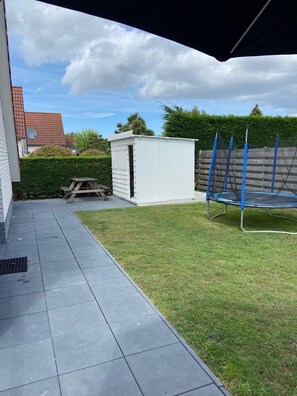 Enjoy a patio with a trampoline, picnic table, and shed, surrounded by a low hedge and wooden fence.