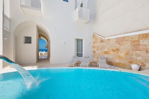 Un área de piscina con vista despejada al mar, un edificio blanco con detalles de piedra y sillas de descanso.