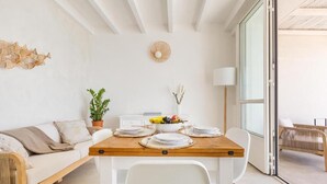 A modern dining area with a wooden table set for four, white chairs, a white sofa, a potted plant, and a decorative wall piece. - Palma Residence Salento (Melendugno)