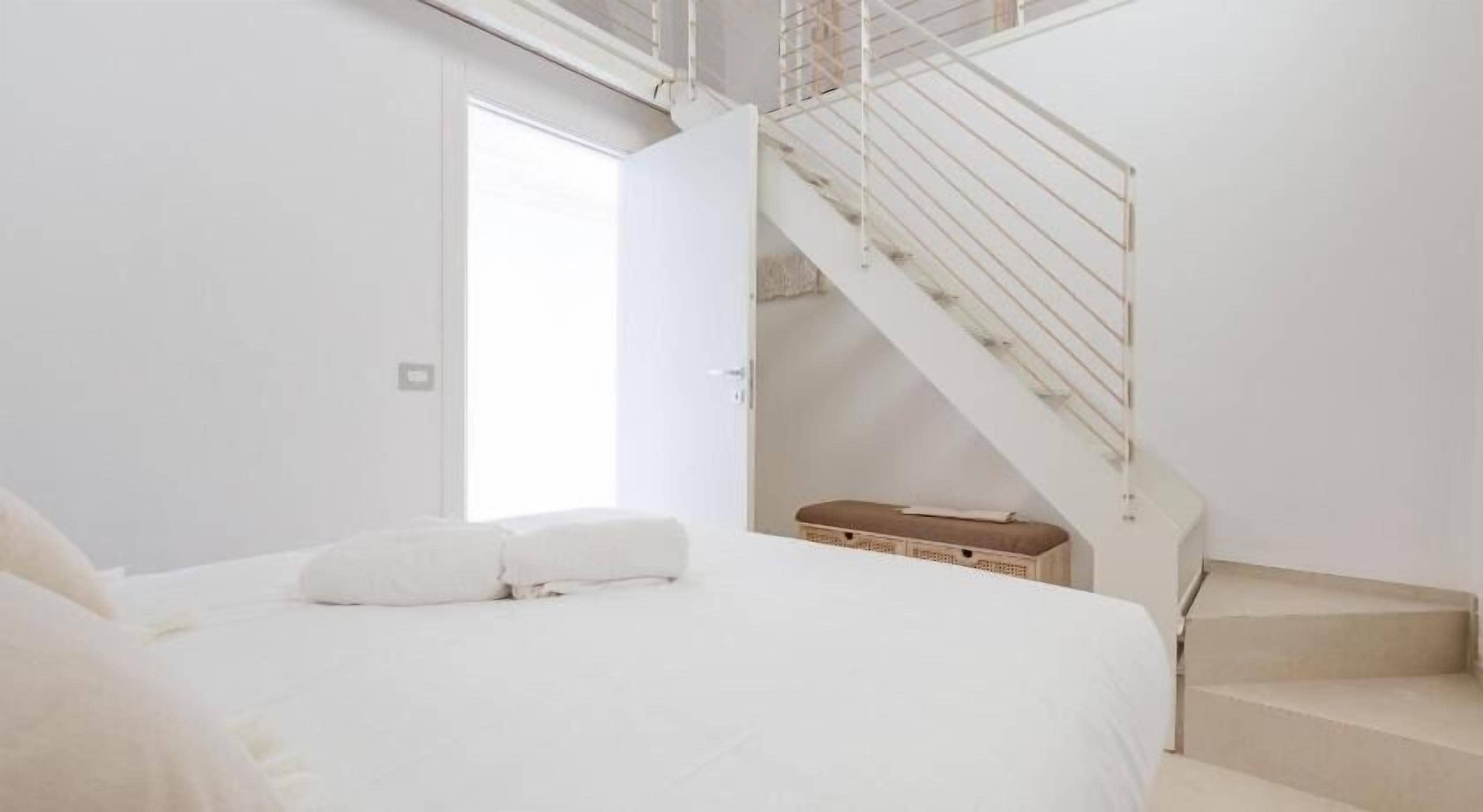A bedroom with a large bed, a suitcase, and a staircase.