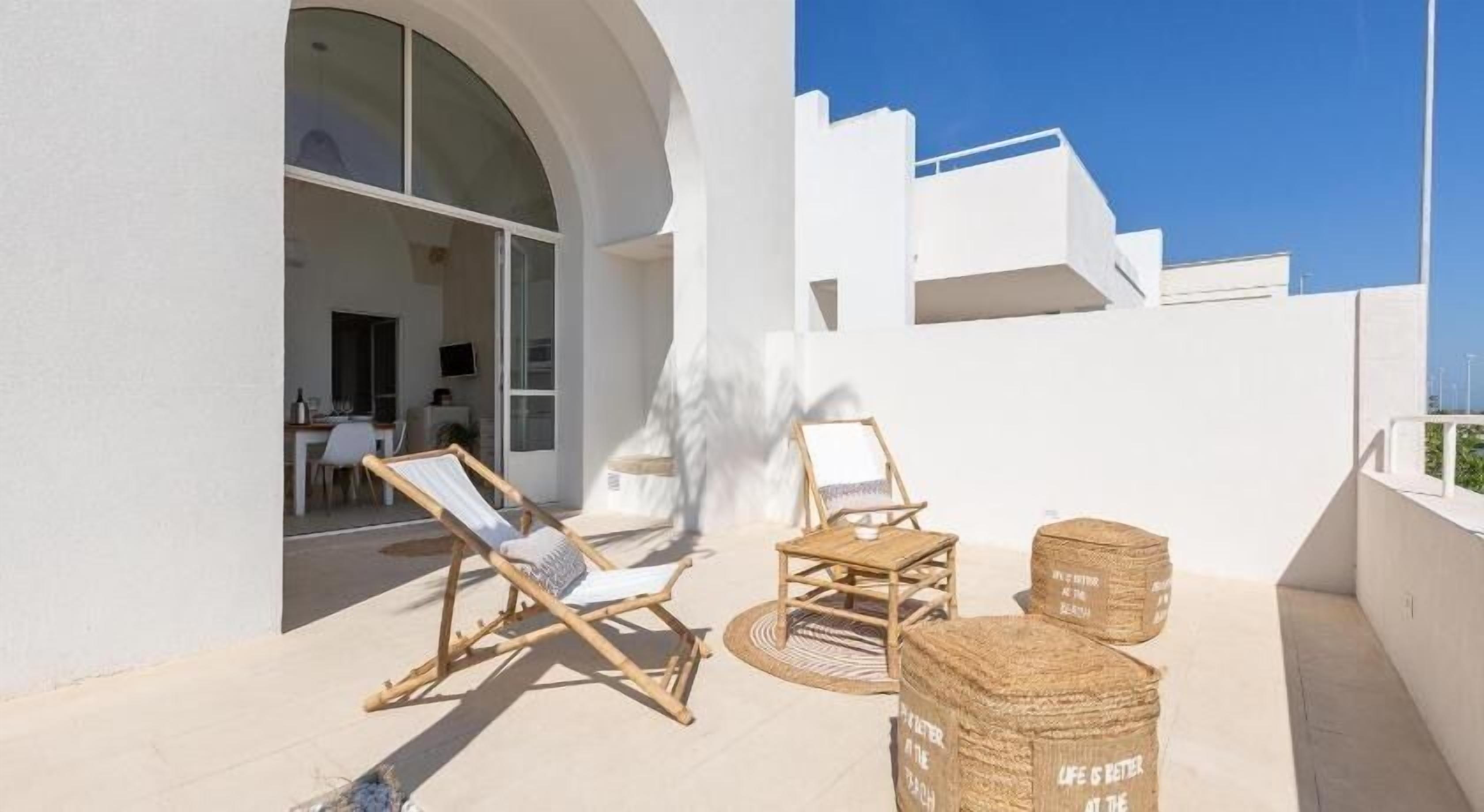 A modern outdoor seating area with wicker furniture and a round table, a large arched doorway, and a clear blue sky.