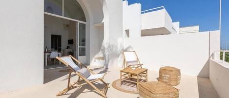 A modern outdoor seating area with wicker furniture and a round table, a large arched doorway, and a clear blue sky.
