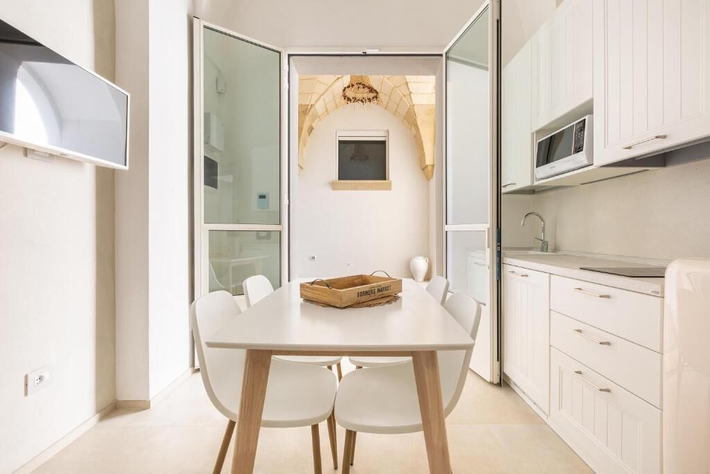 A modern kitchen with white cabinets, a wooden dining table, and a small window above the sink.