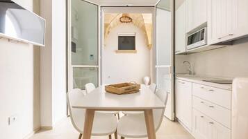 A modern kitchen with white cabinets, a wooden dining table, and a small window above the sink.