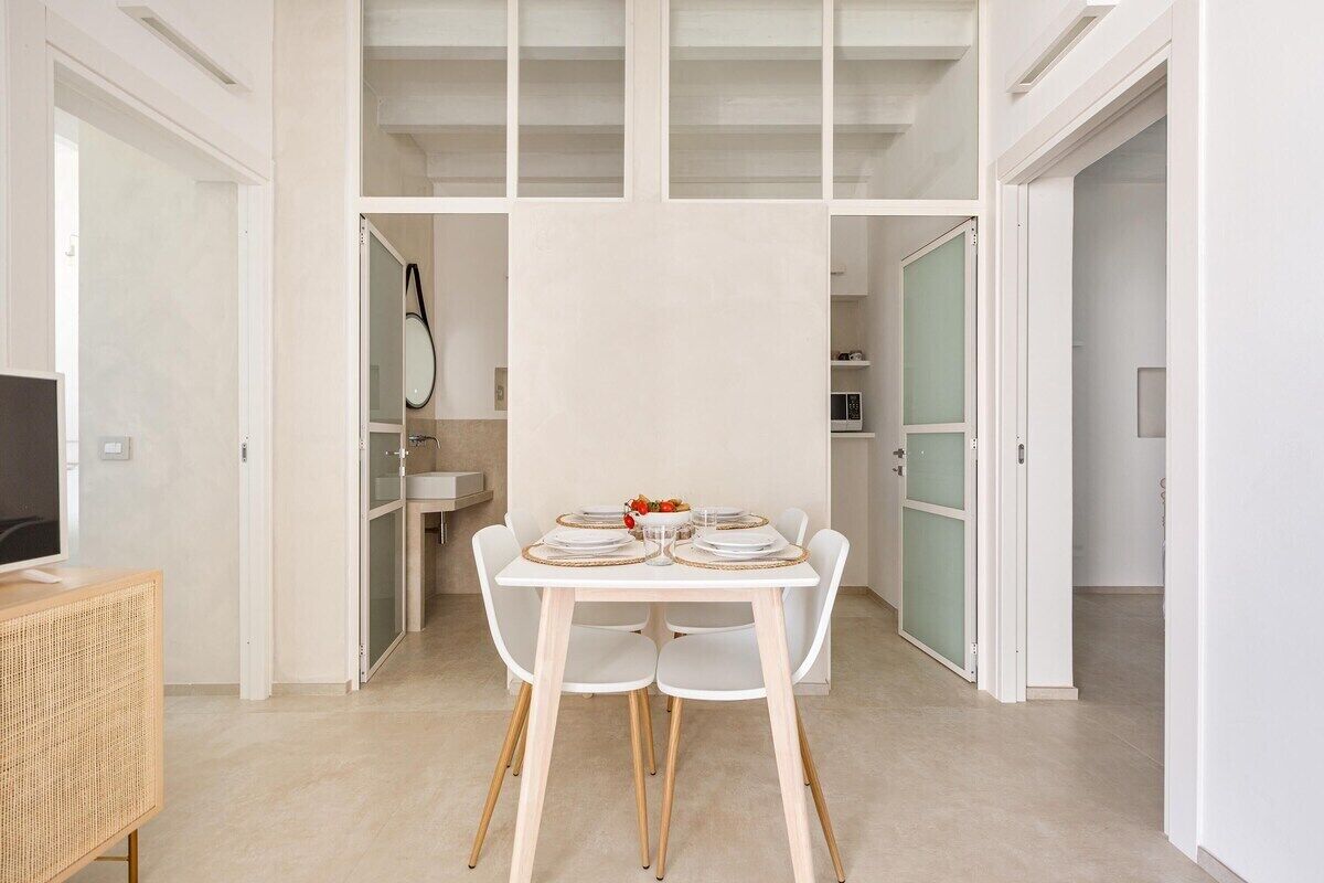 A dining area with a white table set for four, surrounded by white chairs with wooden legs.
