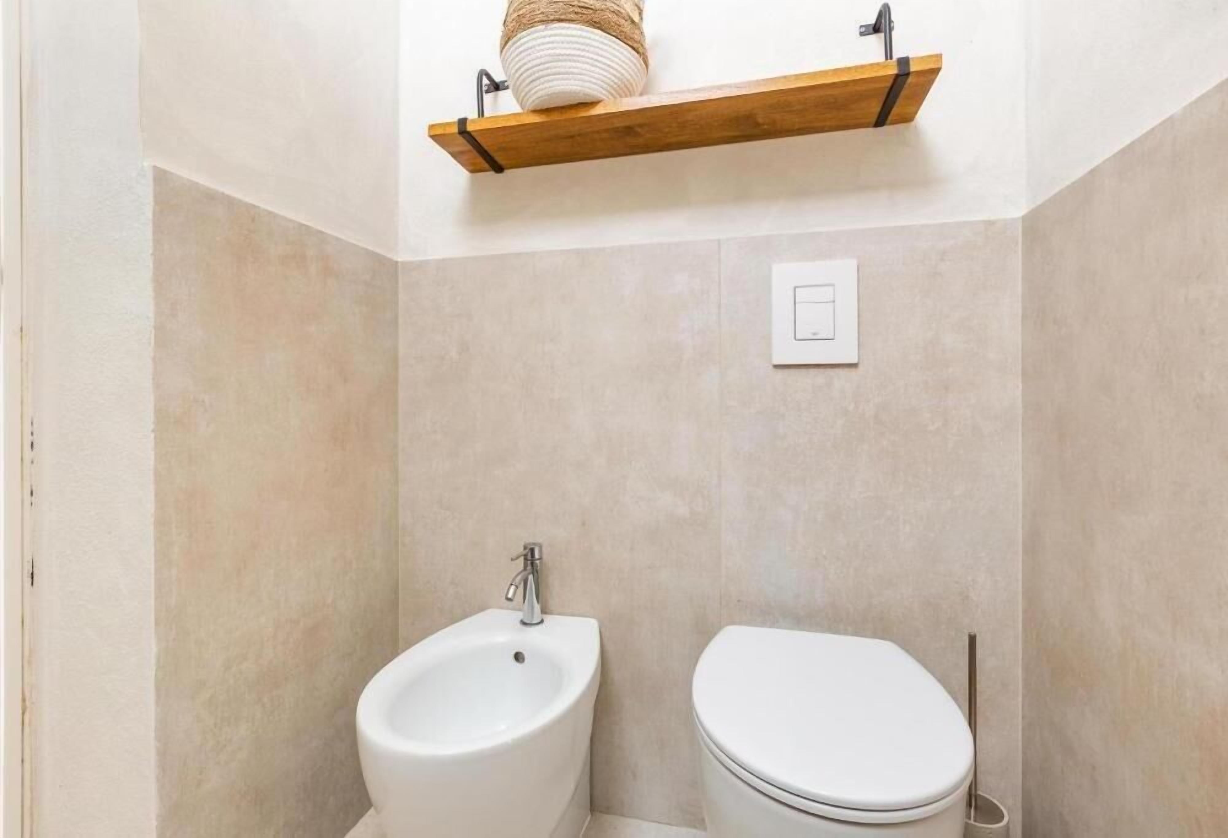 A small bathroom with a white sink, toilet, and a wooden shelf above the sink.