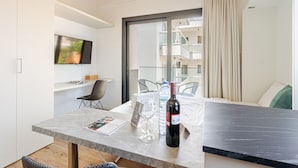 A modern hotel room with a dining area, a TV mounted on the wall, a bottle of wine, and a water bottle on the table. - Yamas Urban Living Platinum Key (Limassol)