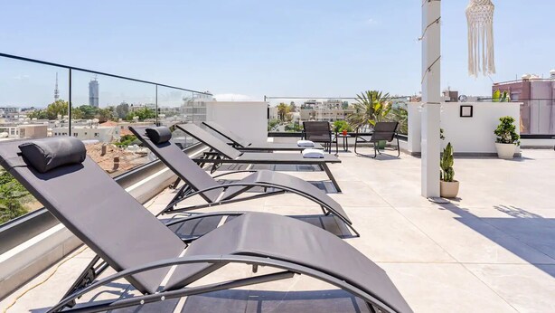 A rooftop terrace with sun loungers, a table with chairs, and potted plants. - Yamas Urban Living Platinum Key (Limassol)