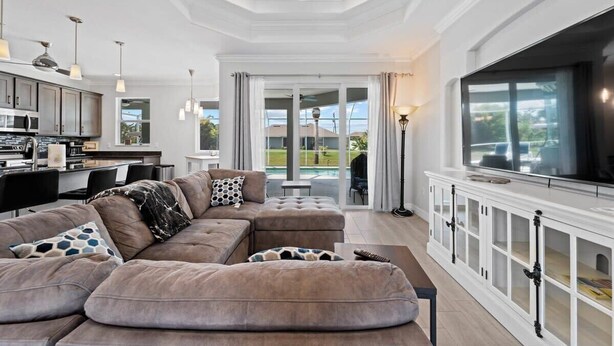 A spacious living area with a large sectional sofa, a television, and a kitchen in the background. - Sun-Soaked & Tranquil Getaway  Relaxing Pool Area (Rotonda West)