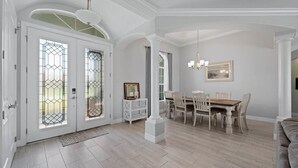 A spacious dining area with a wooden table and chairs, a chandelier, and a white column. - Sun-Soaked & Tranquil Getaway  Relaxing Pool Area (Rotonda West)
