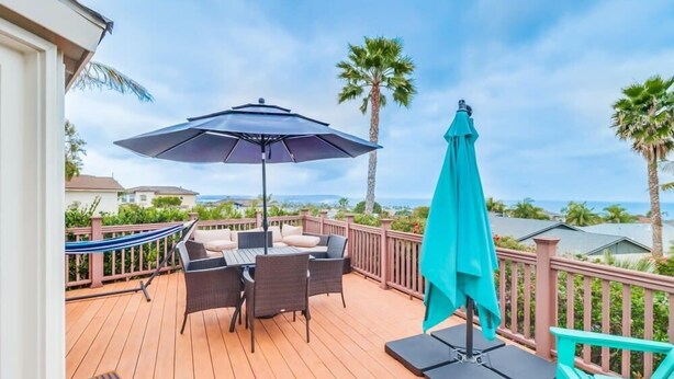A wooden deck with outdoor furniture, including a table and chairs, and two umbrellas.