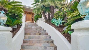 A curved staircase leading to a wooden door, surrounded by lush greenery and a decorative lantern.