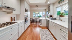 A modern kitchen with white cabinets, a stainless steel range hood, and a dining area with a table and chairs.