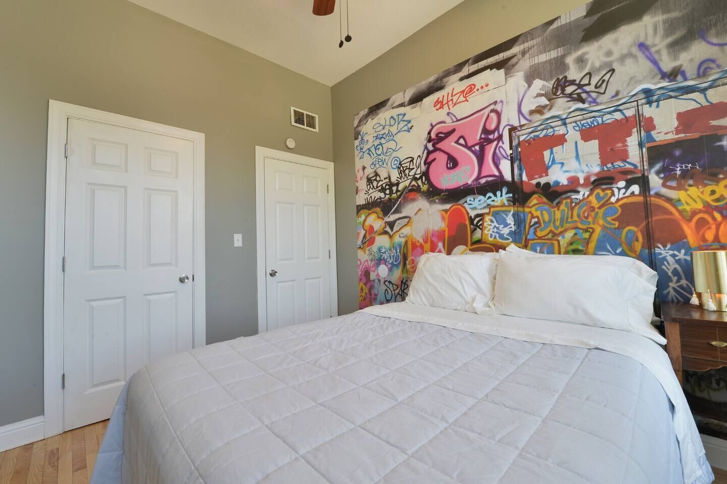 Un dormitorio con cama, dos puertas blancas y una pared cubierta de grafitis.