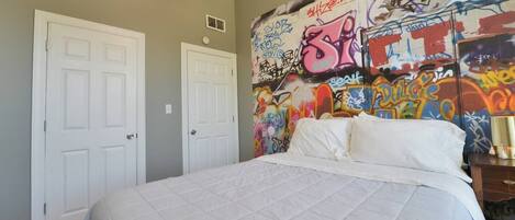 Un dormitorio con cama, dos puertas blancas y una pared cubierta de grafitis.