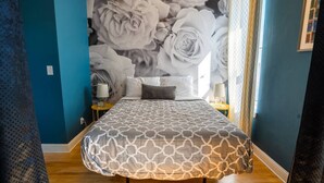 Ein Schlafzimmer mit einem großen Bett, zwei Nachttischen, einer Rosen-Wandmalerei und einem Fenster mit Vorhängen.