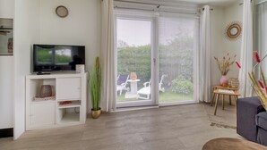Una sala de estar moderna con un televisor de pantalla plana, una planta en maceta y un gran ventanal corredero que da a un patio con mobiliario exterior.
