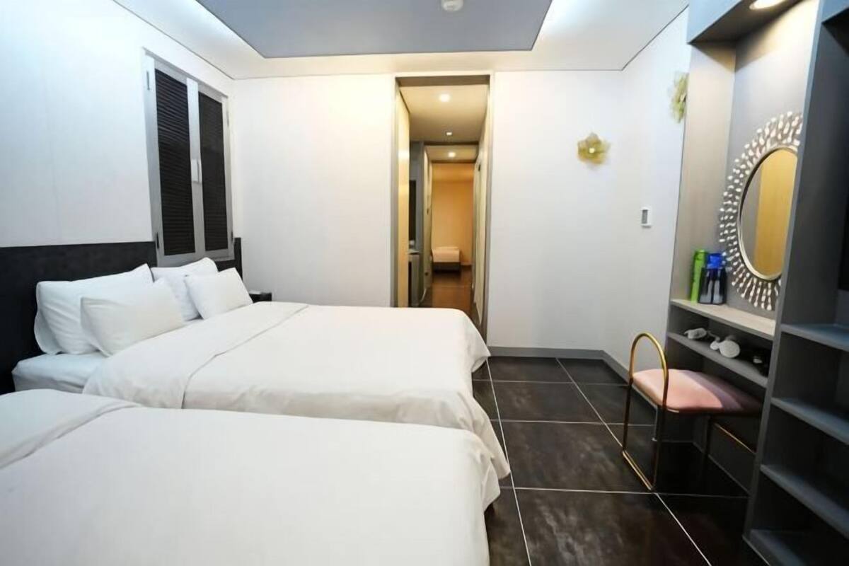 A hotel room with two beds, a vanity with a mirror, and a door leading to a hallway.