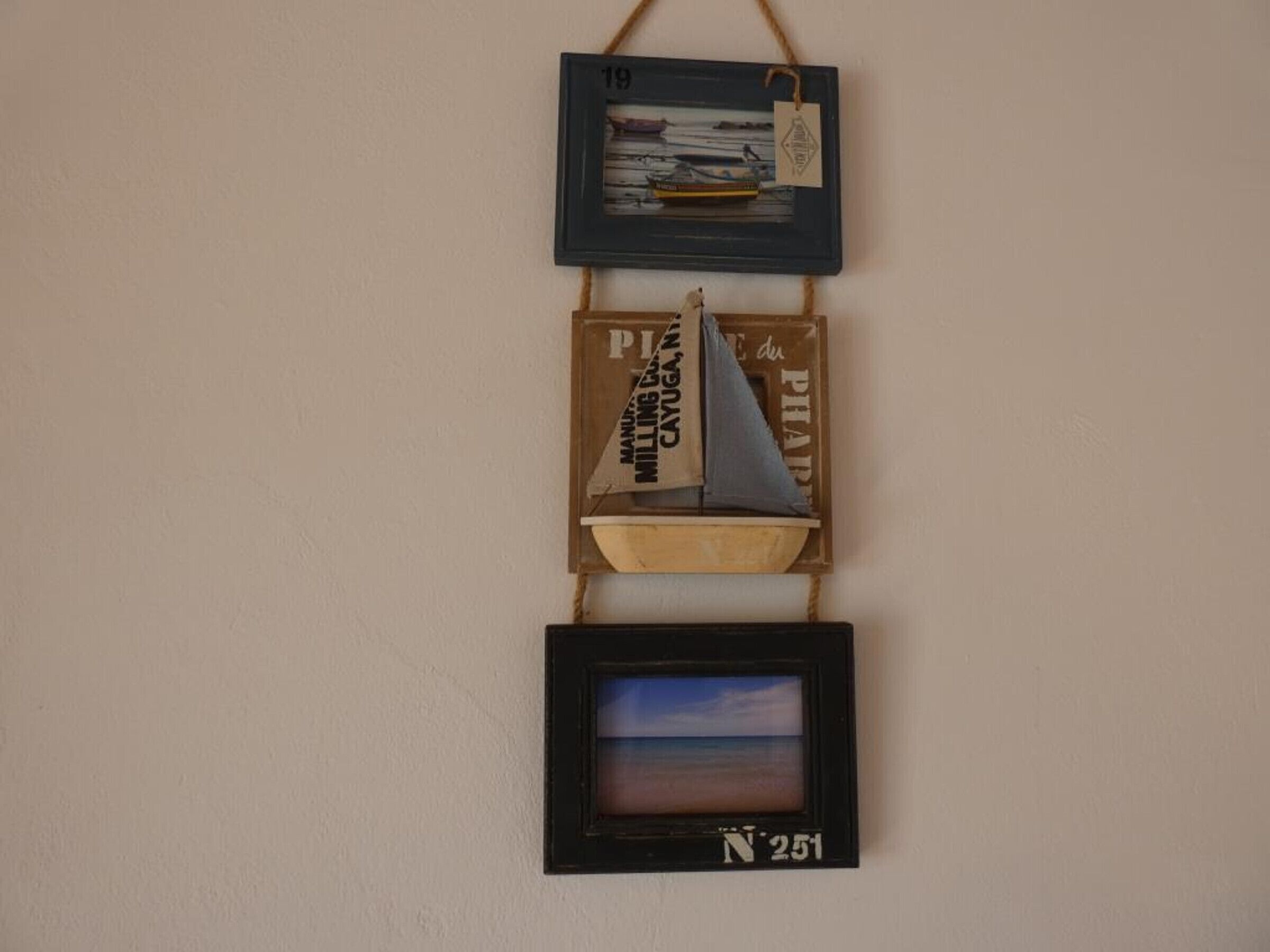 Un mur orné de trois éléments encadrés : une photographie d’un bateau, une enseigne avec du texte et une image encadrée représentant une scène de plage.