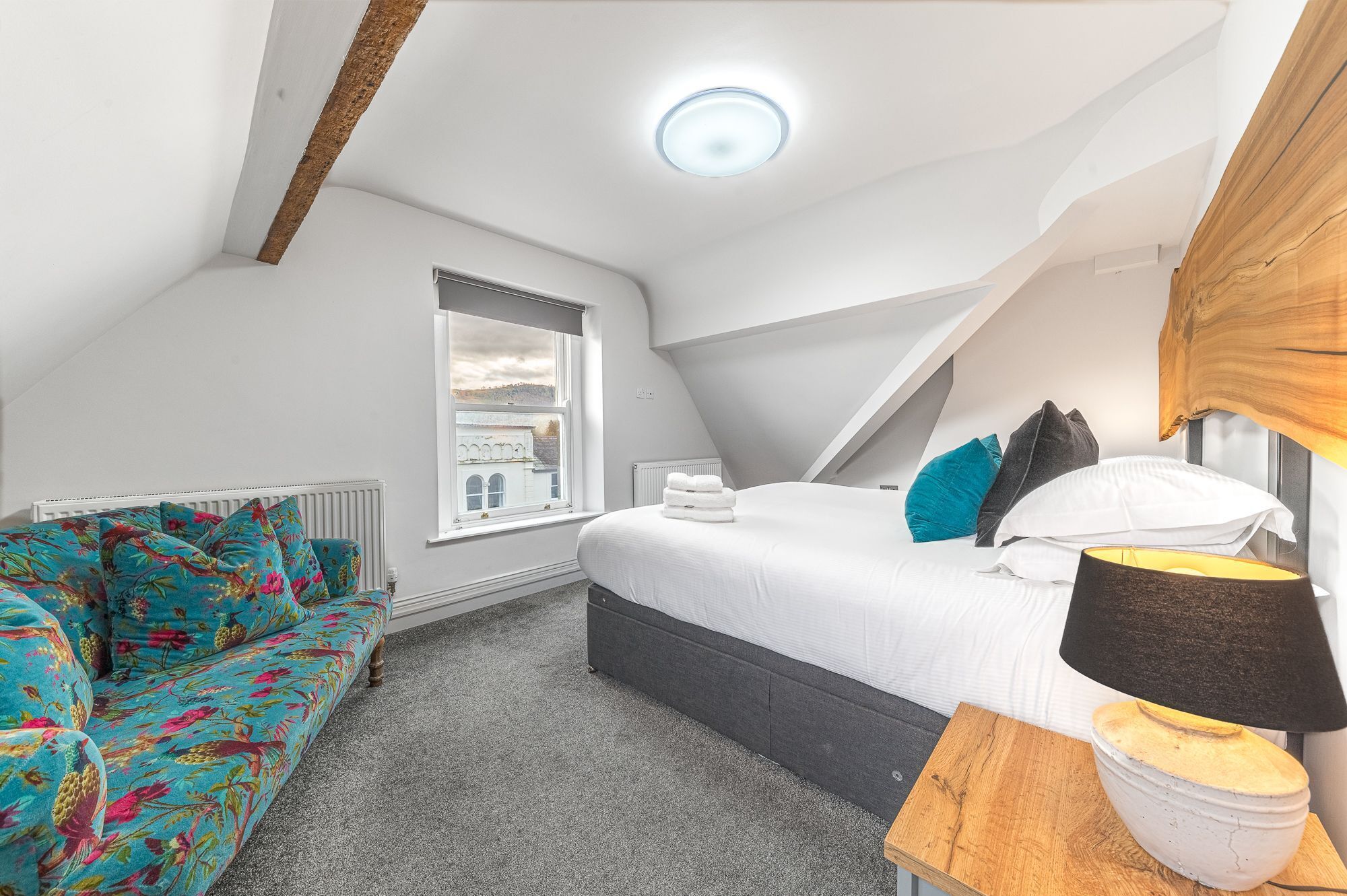 A bedroom with a bed, a window, a radiator, a sofa, and a lamp.
