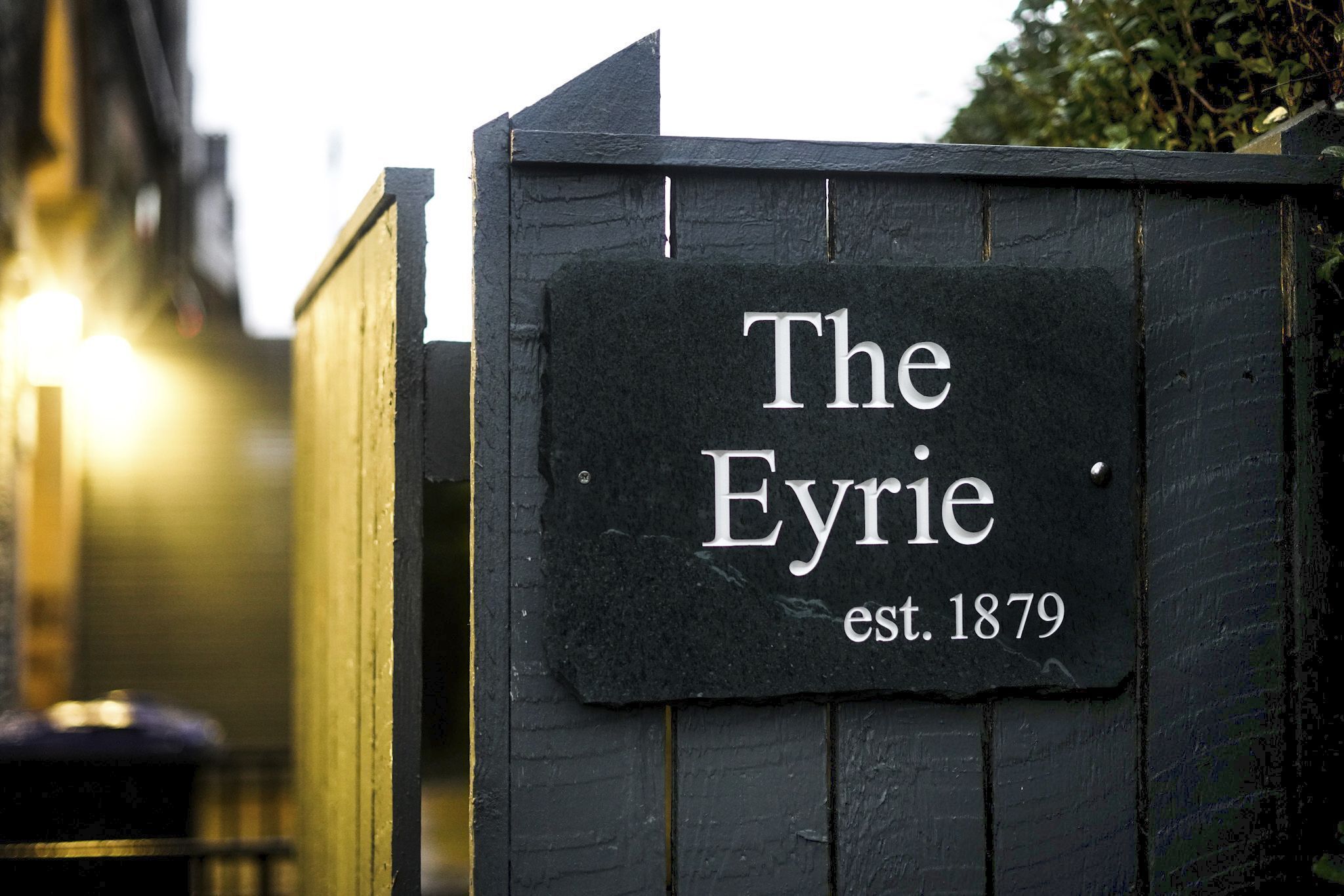 A black wooden sign with white lettering stating "The Eyrie" and "est. 1879".