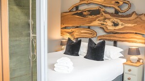 Een slaapkamer met een groot houten hoofdbord, een bed met witte lakens, zwarte kussens en een nachtkastje met een lamp.