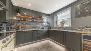Een moderne keuken met donkere kastjes, een marmeren aanrechtblad en een ingebouwde oven.